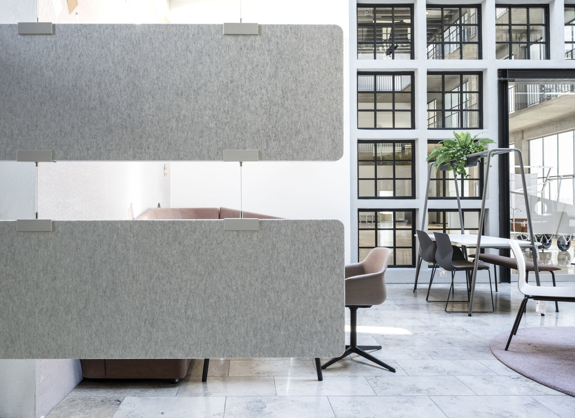 Frameless Baffle Baffle übereinander gehängte graue Akustik-Baffles als vertikaler Raumteiler in einem hellen Atrium mit Loungebereich