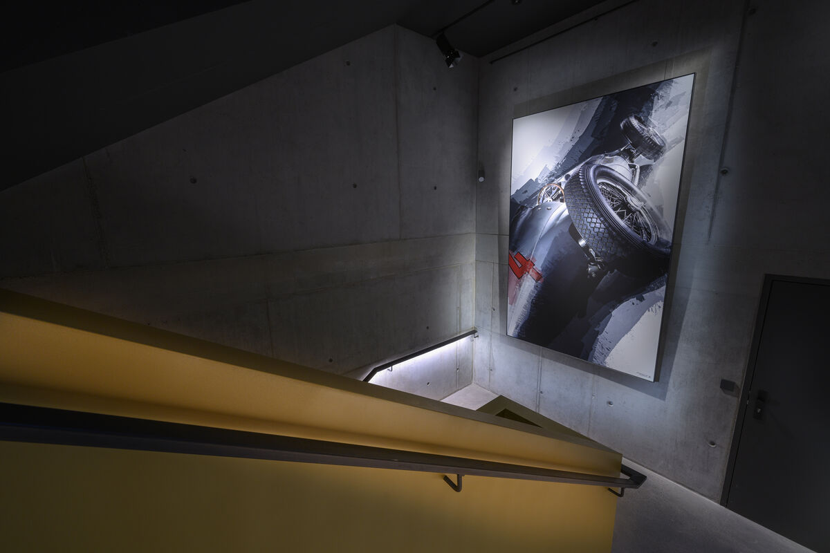 Alu Line Wall beleuchtetes Akustikbild mit bedrucktem Oldtimer-Rennwagen-Motiv als Schallschutz im Sichtbeton-Treppenhaus