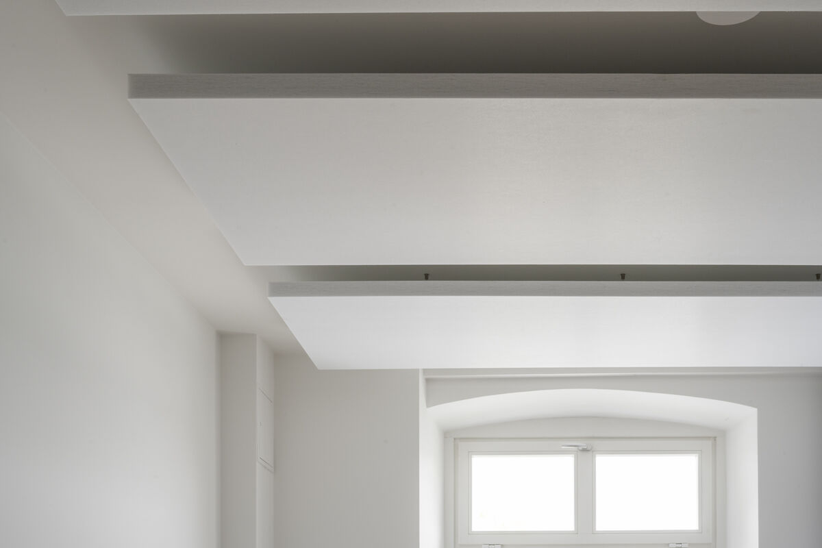 Frameless Sky weiße eckige Akustik-Deckensegel als flächige Schallabsorber an der Decke eines hellen Raums mit Bogenfenster
