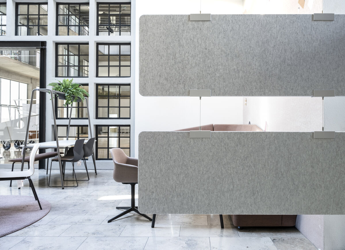 Frameless Baffle Baffle übereinander gehängte graue Akustik-Baffles als Raumteiler vor einem Loungebereich im Atrium