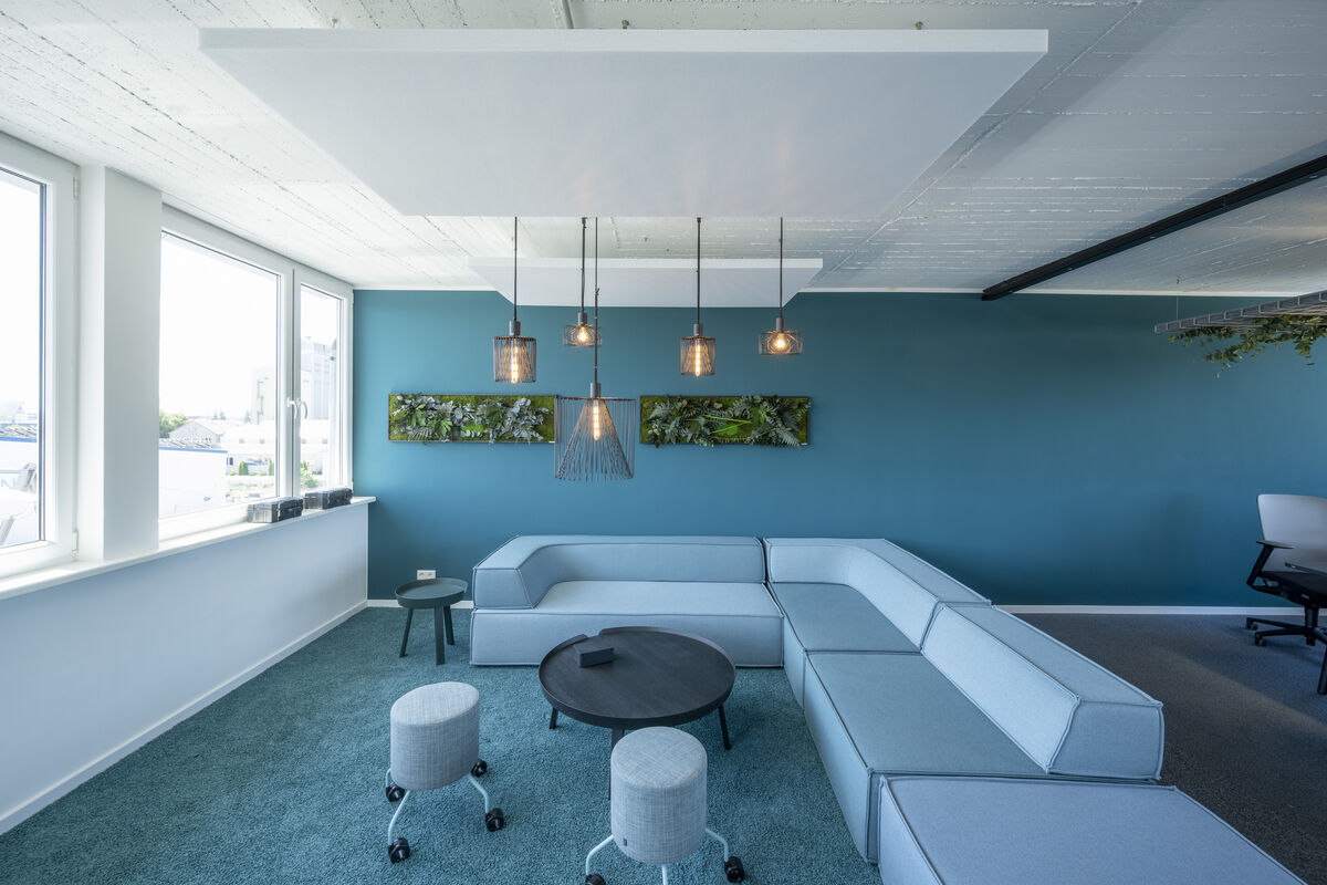 Frameless Sky weißes Akustik-Deckensegel als Schallabsorber über einer blauen Lounge-Sitzecke mit Glaspendelleuchten
