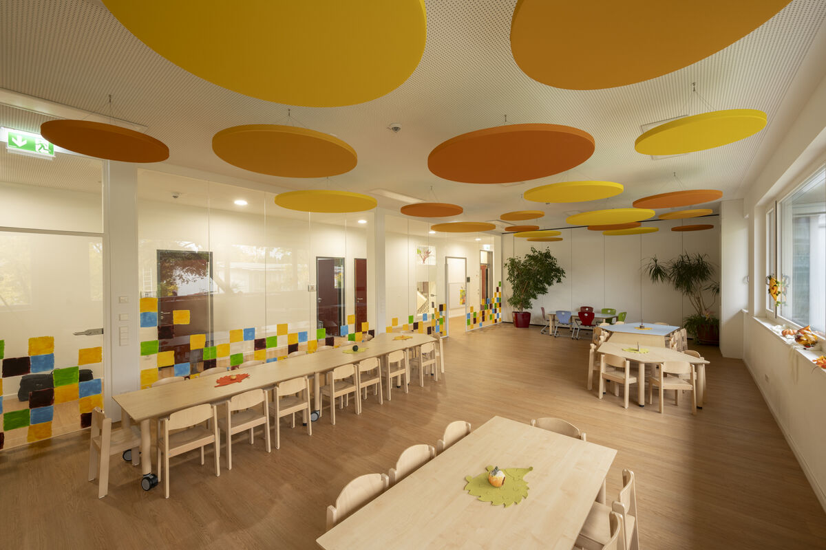 Frameless Color runde farbige Akustik-Deckensegel in Gelb und Orange als Schallschutz im hellen Kita-Gruppenraum mit Holzmöbeln