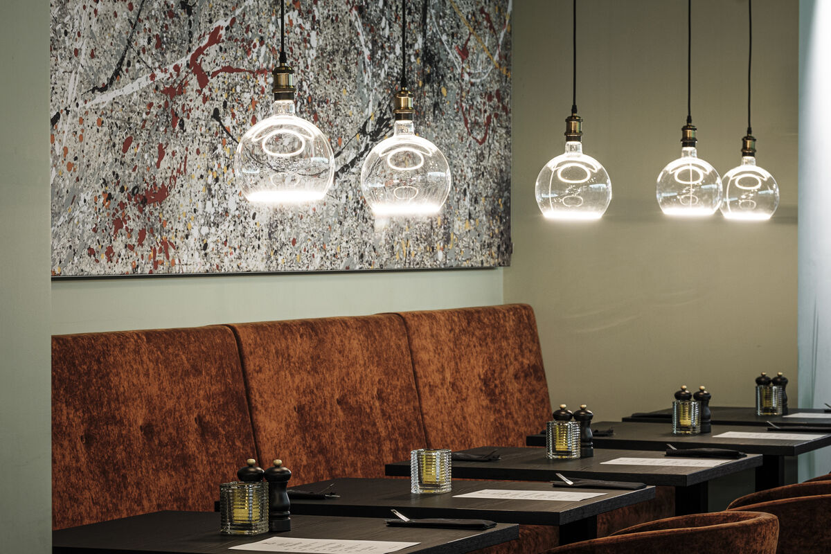Alu Line Wall abstraktes Akustikbild als Schallschutz über einer Sitzbank mit Pendelleuchten im Restaurant