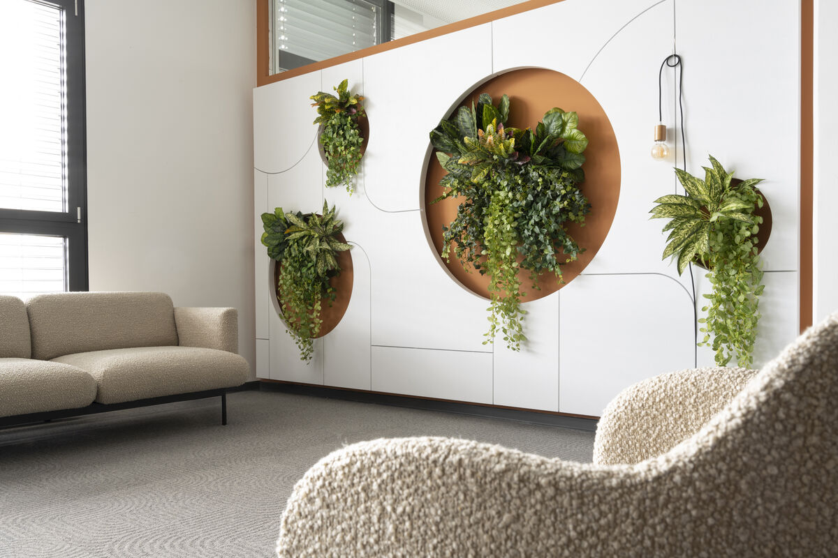 Frameless Custom Cut weiße Akustikwand mit runden Pflanzenausschnitten und Fräsmuster neben einem Loungesofa als Schallschutz